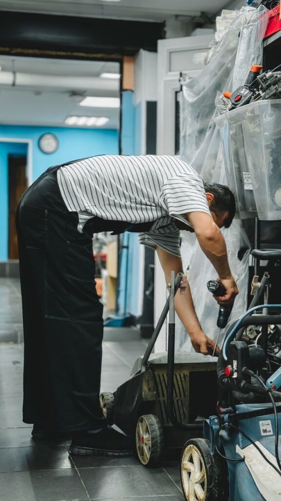 A person fixing a lawn mower in a workshop using a cordless drill.