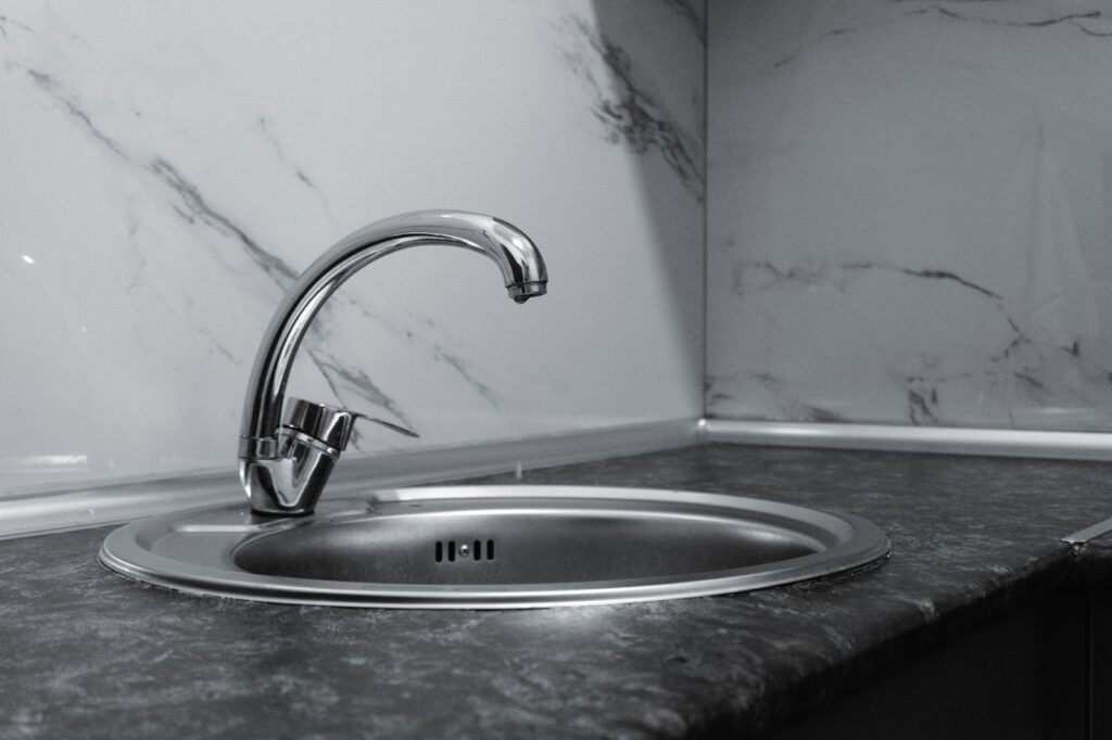 A stylish stainless steel kitchen faucet with a sleek and modern design set against a marble backsplash.